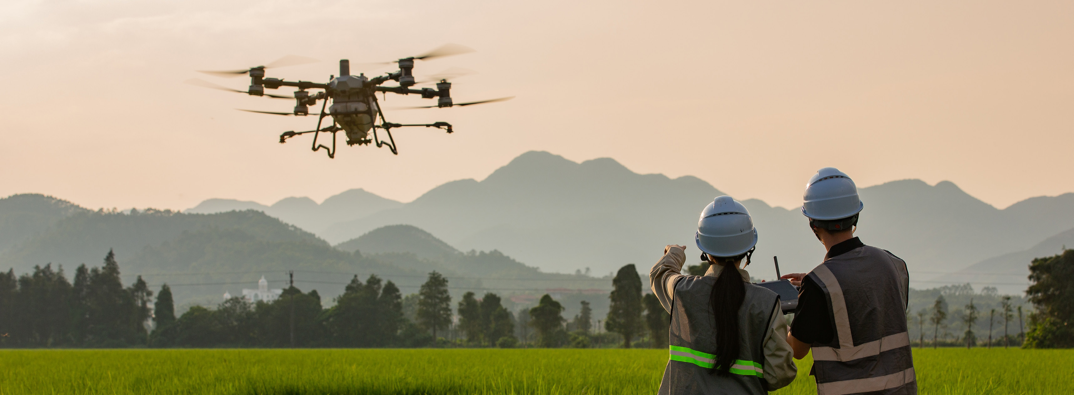 Duas pessoas acompanham um drone agrícola em operação no campo